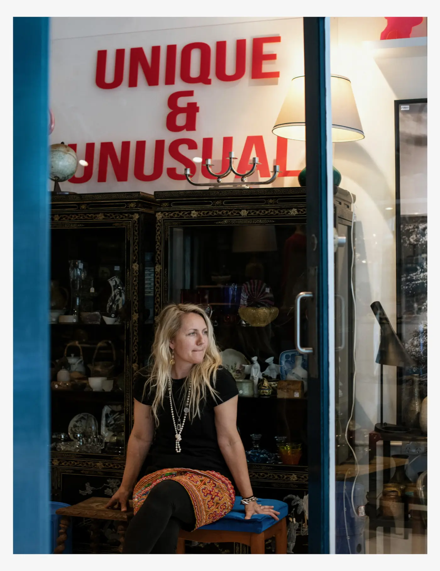 Owner Üüli seated beneath the red Unique & Unusual sign inside her Manly antique shop
